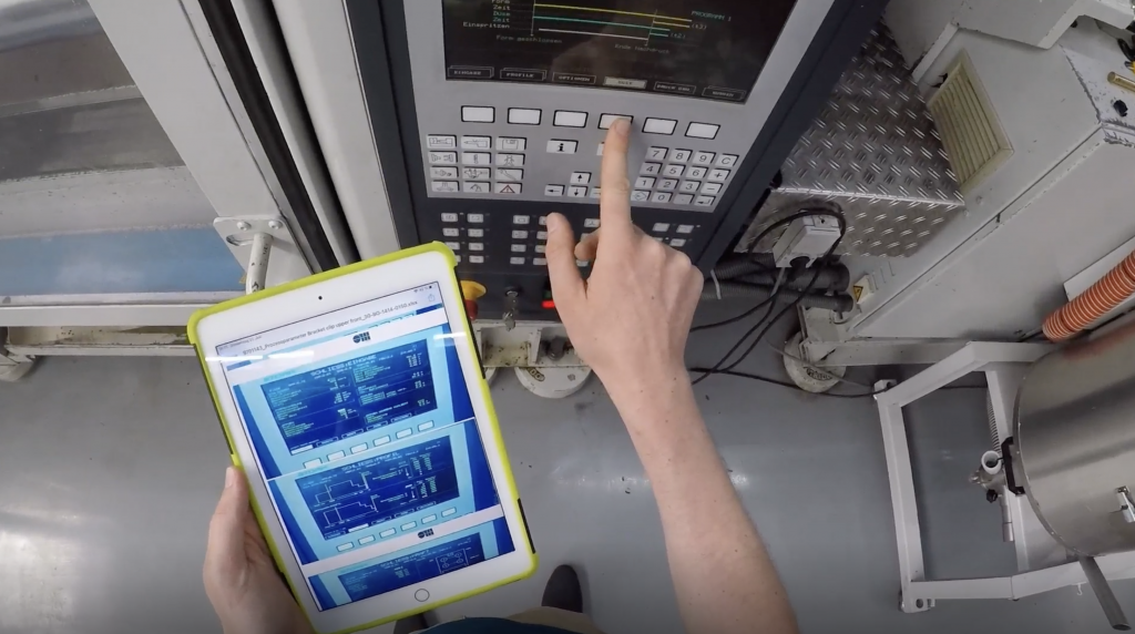 Operator using digital work instructions on a tablet while controlling CNC machine interface in a smart factory.