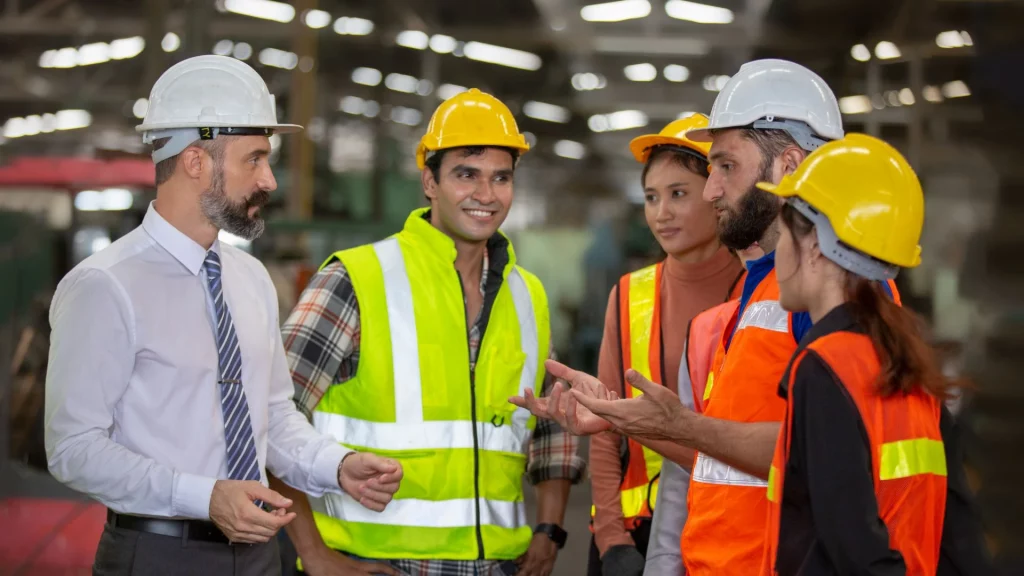 Factory manager discussing safety procedures with industrial workers wearing helmets and safety vests